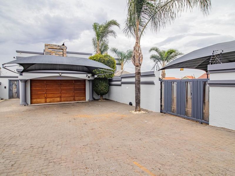 Front exterior view featuring a paved driveway, double garage with wooden door, shade sail carport, and secure perimeter wall with metal gate.