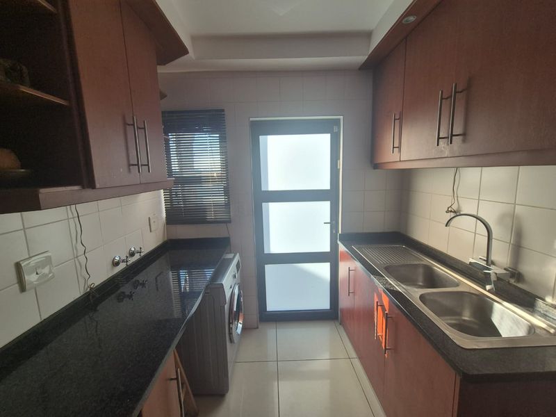 Functional scullery featuring dark granite countertops, ample built-in cabinetry, double stainless steel sink, and direct access to the exterior via a frosted glass door.