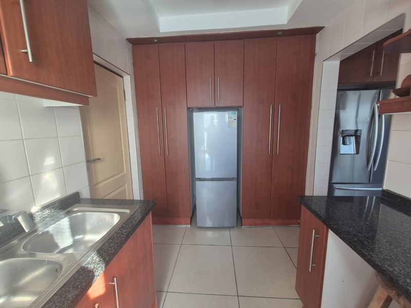 A functional kitchen featuring dark wood cabinetry, granite countertops, a double stainless steel sink, and tiled flooring with integrated storage space.