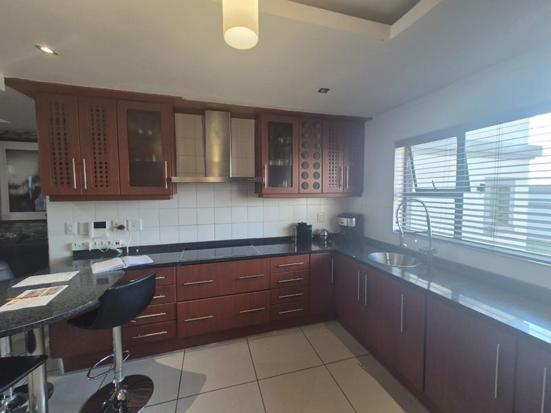 A functional kitchen featuring dark wood cabinetry, granite countertops, a tiled backsplash, and integrated stainless steel appliances with a breakfast bar area.