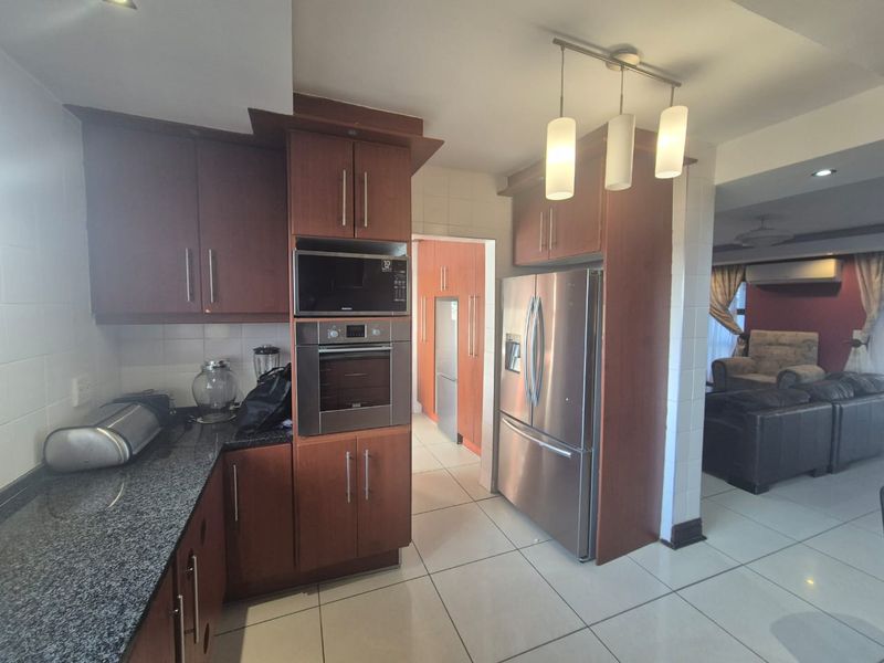 A functional kitchen featuring dark wood cabinetry, granite countertops, built-in oven and microwave, and tiled flooring, with an adjacent scullery area.