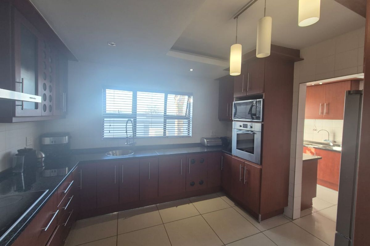 A functional kitchen featuring dark wood cabinetry, granite countertops, built-in stainless steel appliances, and tiled flooring, with an adjacent scullery area.