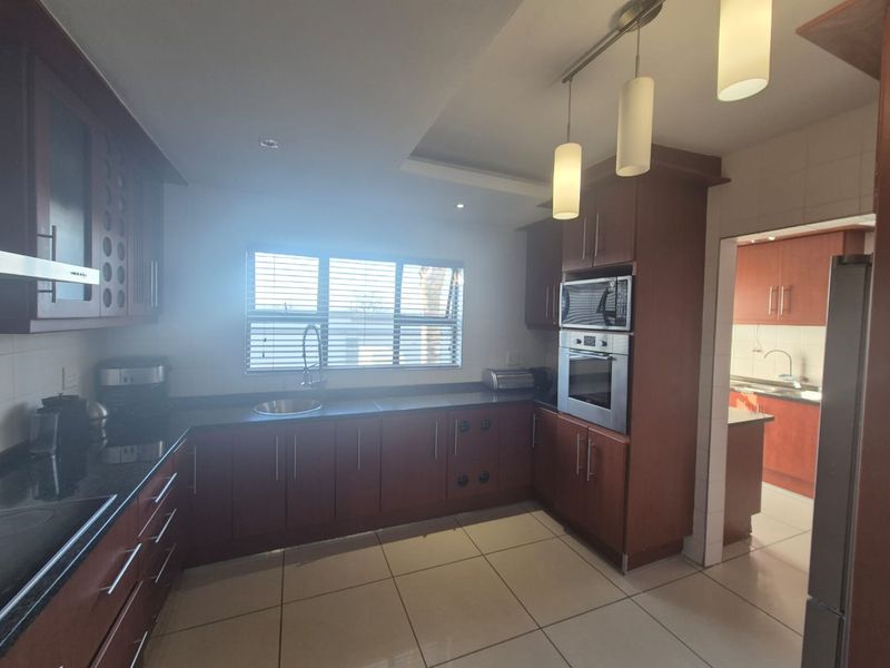 A functional kitchen featuring dark wood cabinetry, granite countertops, built-in stainless steel appliances, and tiled flooring, with an adjacent scullery area.