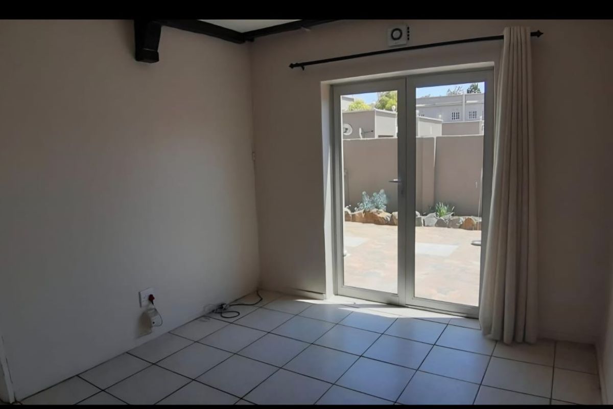 An empty living room featuring tiled flooring, exposed ceiling beams, and double glass doors providing direct access to the rear patio area.