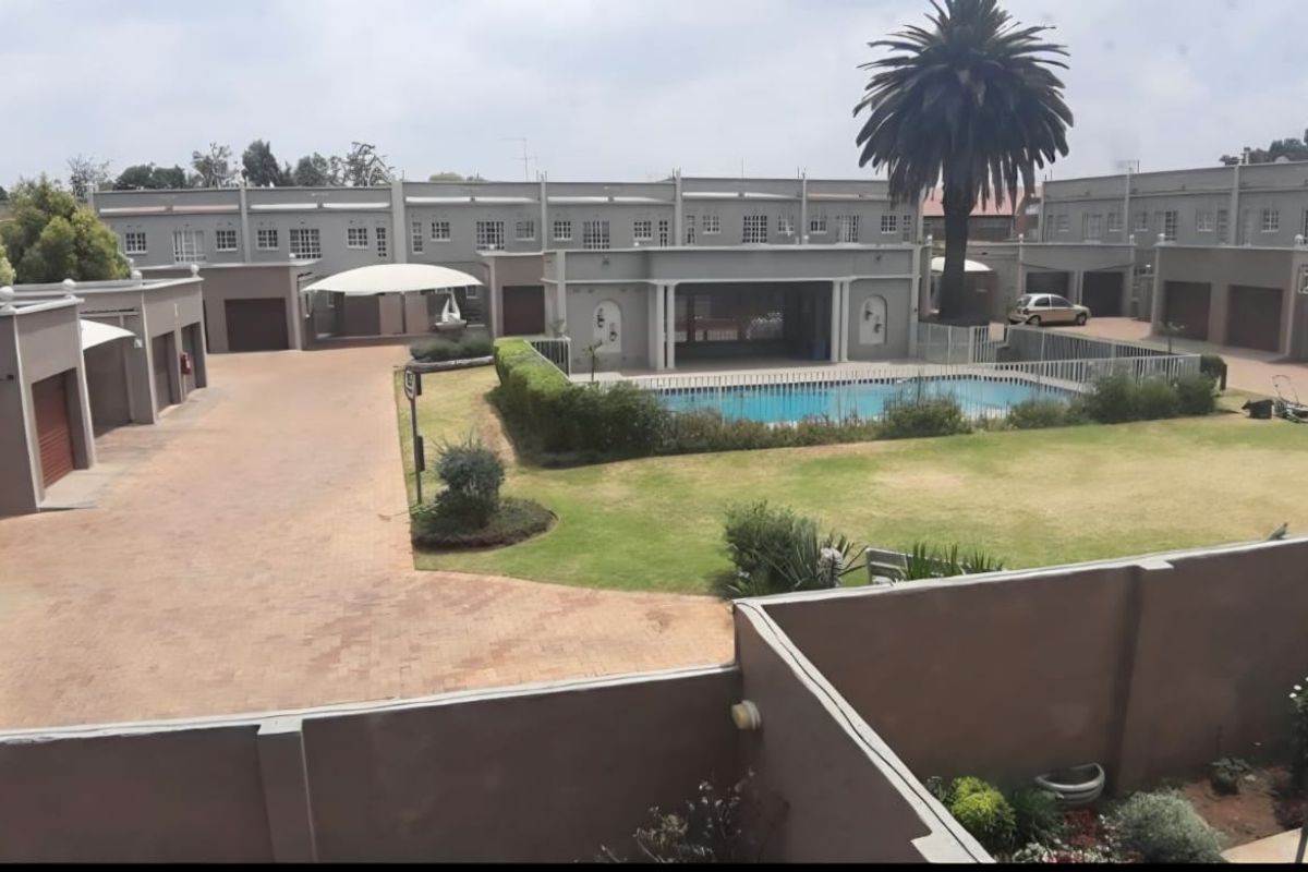 Aerial view of a townhouse complex featuring a central swimming pool, landscaped gardens, paved driveways, and multiple garage units.
