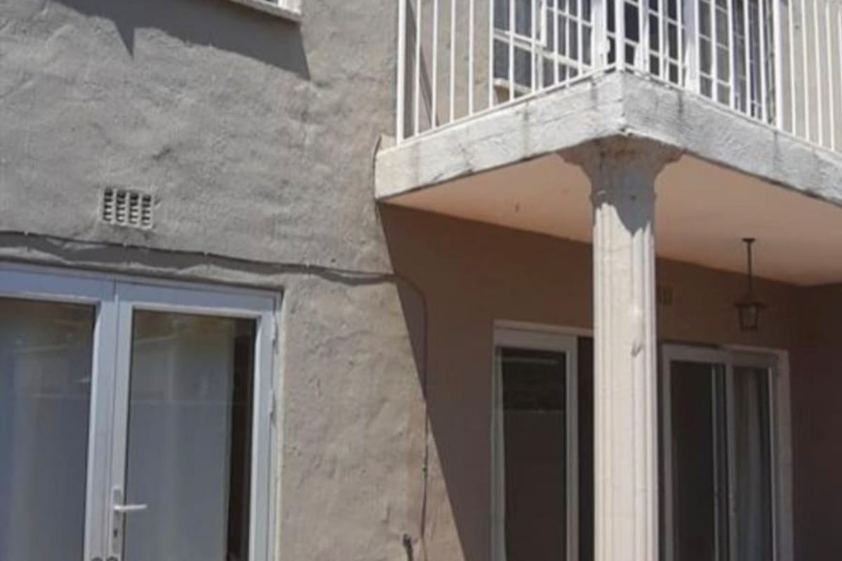 Rear exterior view of the townhouse featuring a tiled patio, a balcony with metal railing, and sliding door access to the interior.