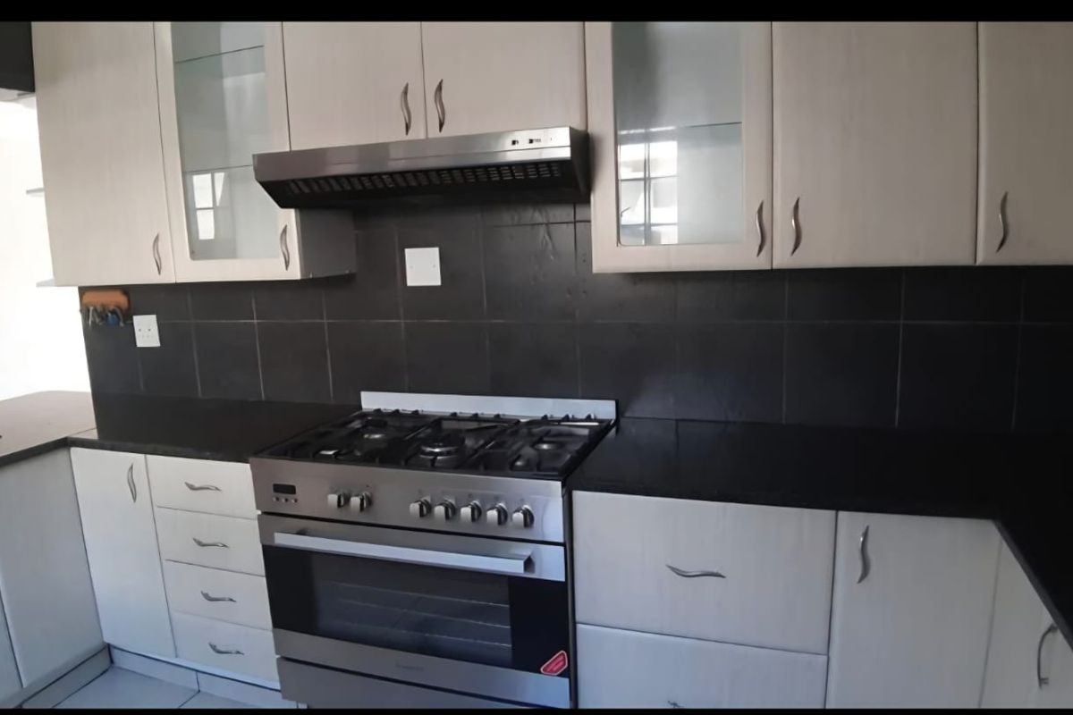 A functional kitchen featuring light-toned cabinetry, dark granite countertops, a gas stove with an extractor fan, and a contrasting tiled backsplash.