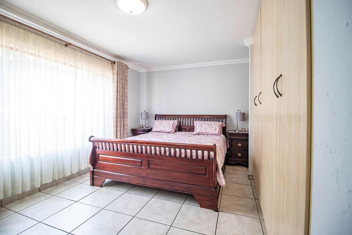 A well-lit bedroom featuring neutral tiled flooring, built-in wooden cupboards, and decorative ceiling cornicing.