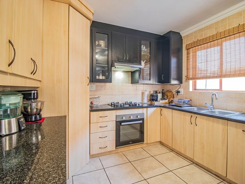 Functional kitchen featuring a mix of light wood and dark cabinetry, granite countertops, gas hob, built-in oven, and tiled finishes.