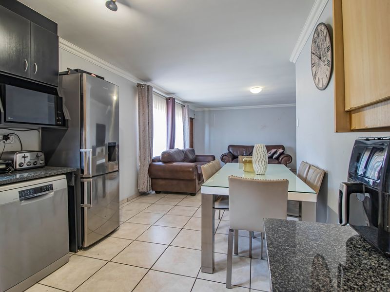 Open-plan kitchen and dining area featuring tiled flooring, granite countertops, and built-in cabinetry, flowing into a comfortable living space.