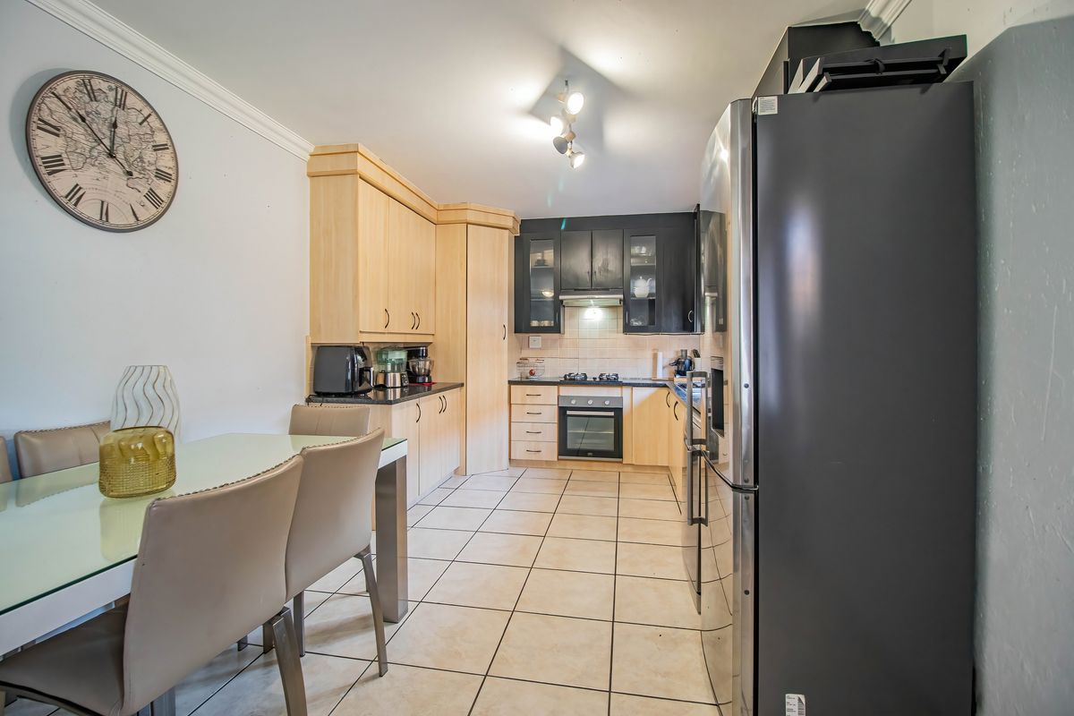 A functional kitchen featuring a mix of light wood and dark cabinetry, built-in oven and hob, and tiled flooring, with an adjacent dining area.