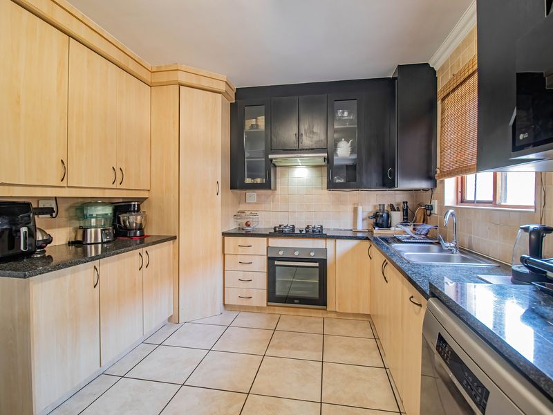 A functional kitchen featuring a mix of light wood and dark cabinetry, granite countertops, built-in oven, gas hob, and tiled flooring.