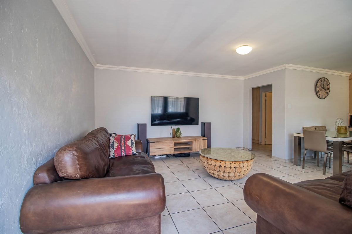 A spacious living room featuring neutral tiled flooring, crisp white walls, and decorative ceiling cornicing, providing a comfortable and functional living space.