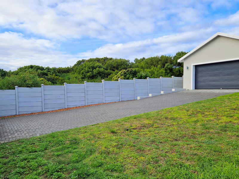 A clean exterior view featuring a paved driveway leading to a double garage, enclosed by a neat precast concrete boundary wall.