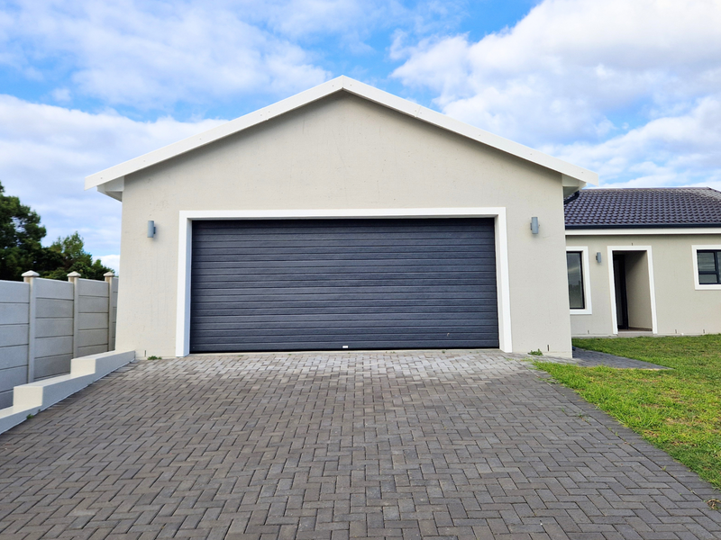 Front view of a modern house featuring a paved driveway, a dark sectional garage door, and a clean, well-maintained exterior facade.
