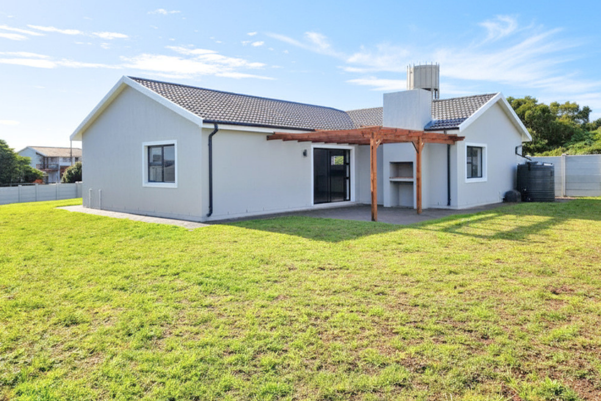 Rear view of a modern house featuring a spacious lawn, a built-in braai area, a wooden pergola, and a water tank.