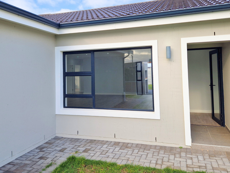 A clean rear exterior view featuring a paved patio area, modern aluminium window and door frames, and a neutral rendered facade.