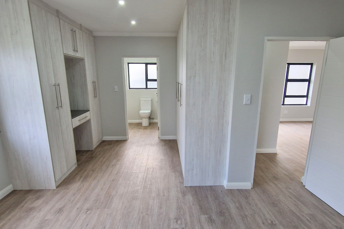 Modern bedroom featuring extensive built-in cupboards, light wood-look laminate flooring, and direct access to an en-suite bathroom.