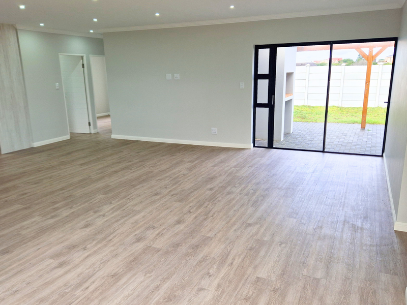 Spacious open-plan living area featuring modern laminate flooring, recessed lighting, and large sliding glass doors providing seamless access to the outdoor patio.