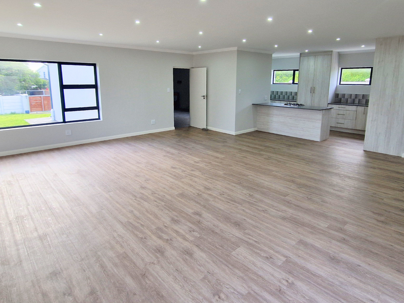 Spacious open-plan living area featuring modern laminate flooring, recessed lighting, and a contemporary kitchen with a central island and built-in cabinetry.