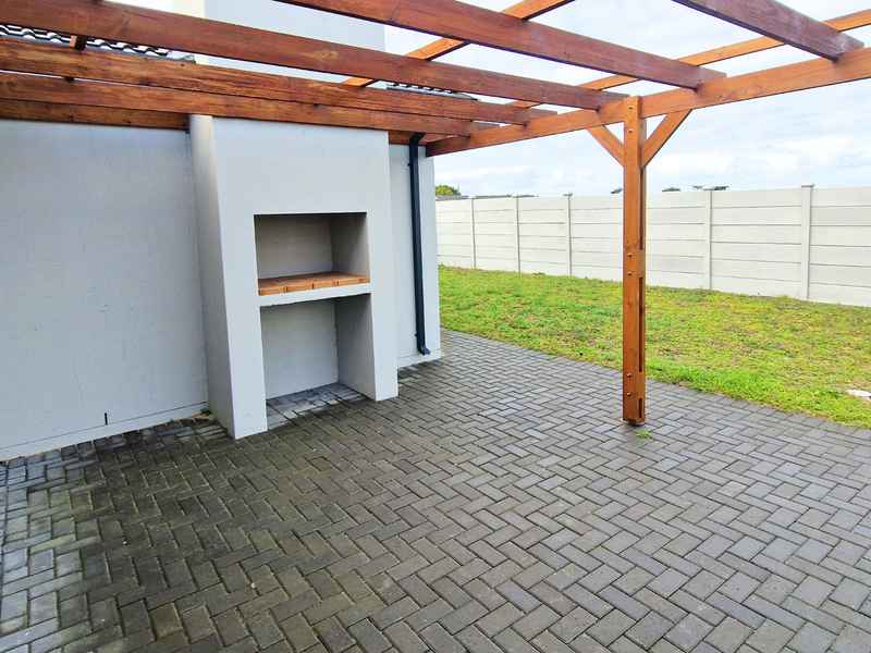 Outdoor patio area featuring a timber pergola and a built-in braai, overlooking a private garden with a precast concrete boundary wall.