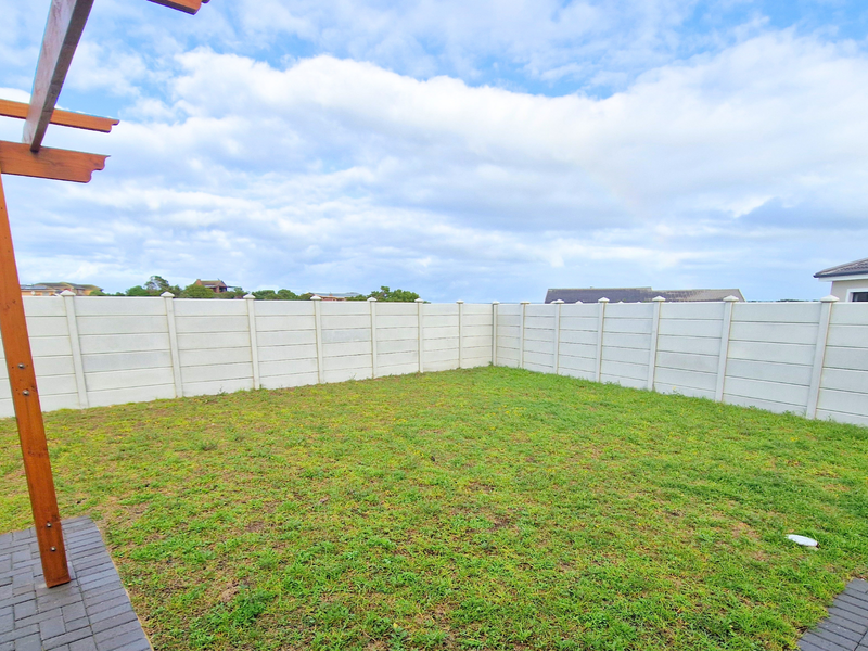 A private rear garden featuring a paved patio area, a timber pergola, and a secure precast concrete boundary wall.