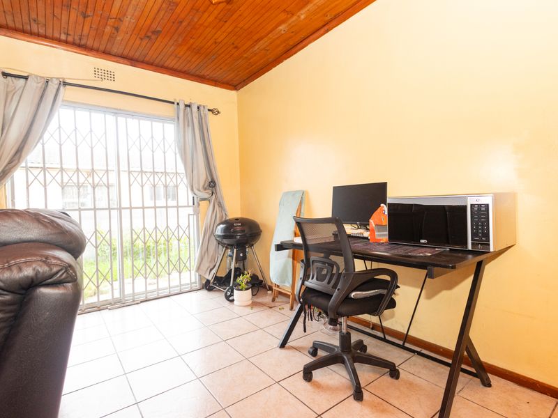 A living area featuring tiled flooring, a timber-clad ceiling, and a sliding glass door with a security gate providing access to the exterior.