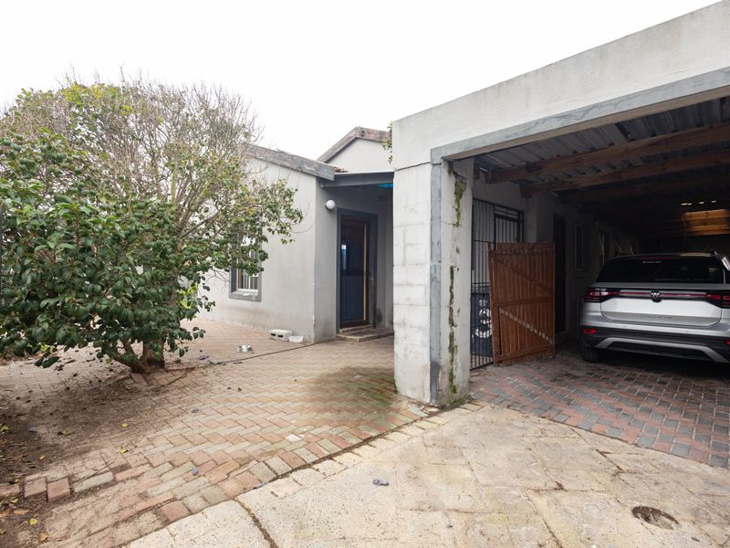 Front exterior view featuring a paved driveway, carport structure, and entrance area with visible wear on the paving and exterior finishes.
