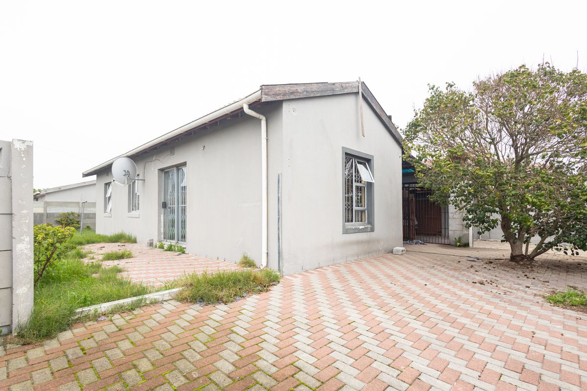 Rear view of the property featuring a paved driveway, security gate, and exterior wall with guttering and satellite dish installation.