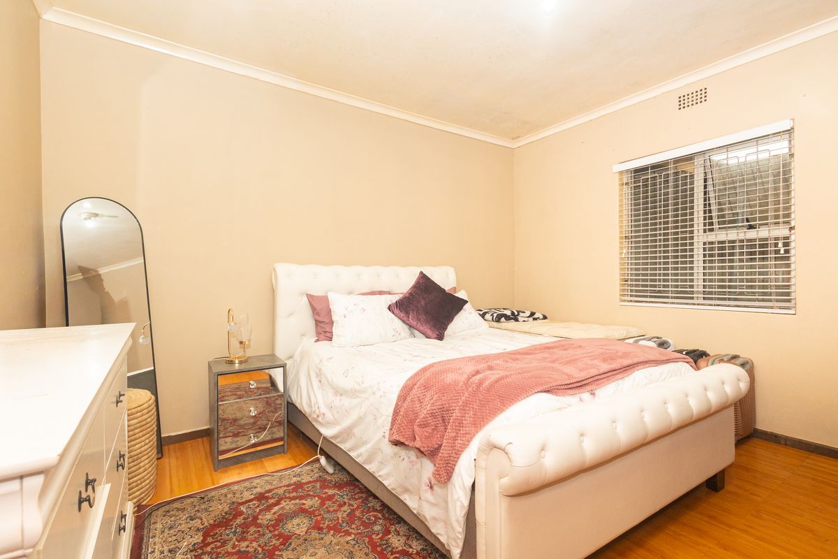 A standard bedroom featuring laminate flooring, a window with security bars, and coved ceilings. The room requires minor cosmetic updates to the walls and ceiling.
