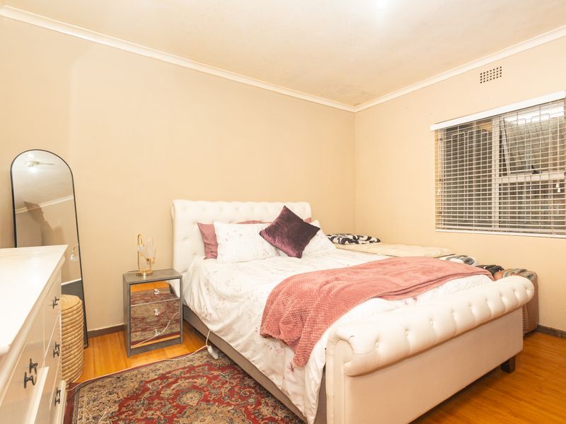 A standard bedroom featuring laminate flooring, a window with security bars, and coved ceilings. The room requires minor cosmetic updates to the walls and ceiling.