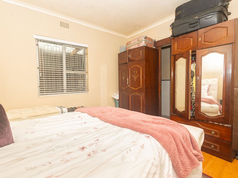 A bedroom featuring laminate flooring, security bars on the window, and ceiling cornicing, currently showing signs of wear and dated finishes.