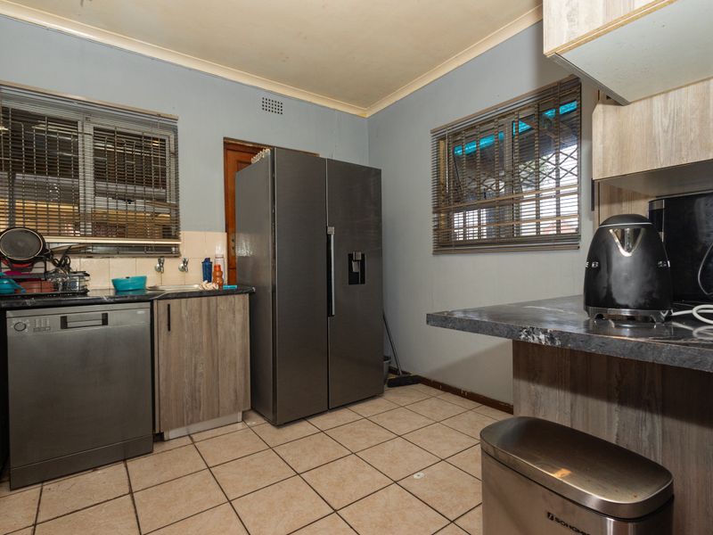 A functional kitchen featuring laminate cabinetry, tiled flooring, and integrated appliances, currently showing signs of wear and requiring cosmetic updates.