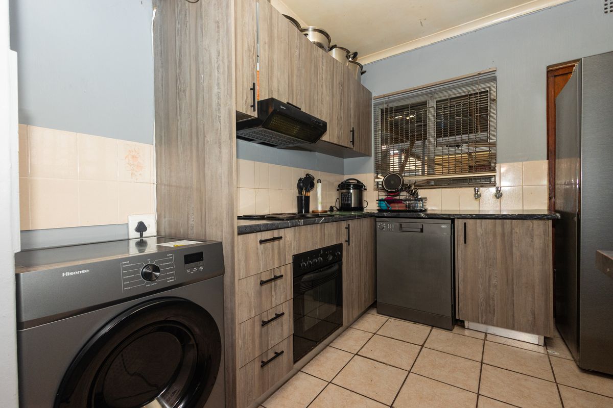 A functional kitchen featuring wood-look laminate cabinetry, built-in oven, extractor fan, and tiled flooring with a neutral backsplash.
