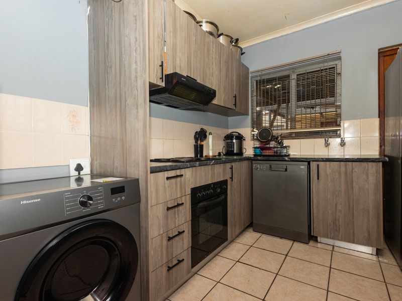 A functional kitchen featuring wood-look laminate cabinetry, built-in oven, extractor fan, and tiled flooring with a neutral backsplash.