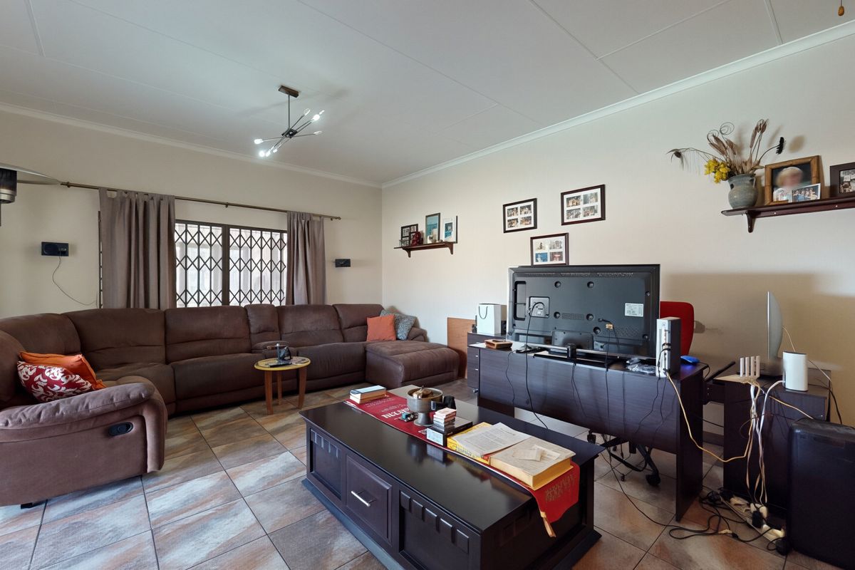 A spacious living room featuring tiled flooring and a security gate on the window, providing a functional and comfortable family living space.