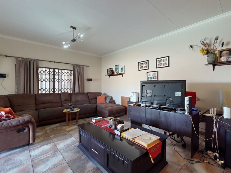 A spacious living room featuring tiled flooring and a security gate on the window, providing a functional and comfortable family living space.