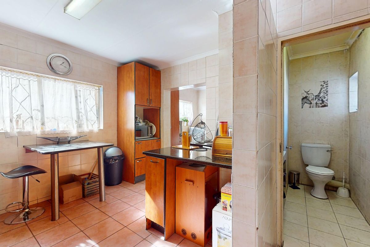 A dated kitchen featuring tiled walls and flooring, built-in cabinetry, and a granite countertop, with an adjacent small bathroom area.