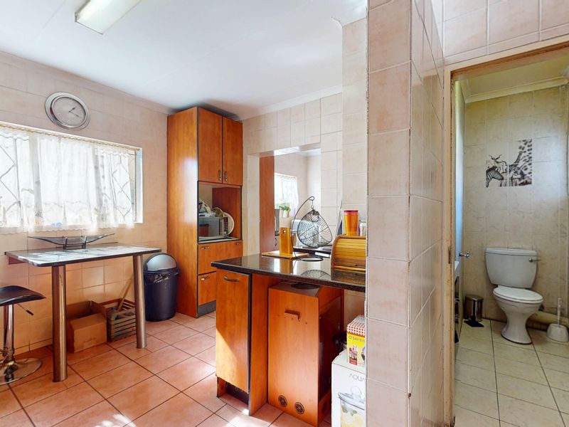 A dated kitchen featuring tiled walls and flooring, built-in cabinetry, and a granite countertop, with an adjacent small bathroom area.