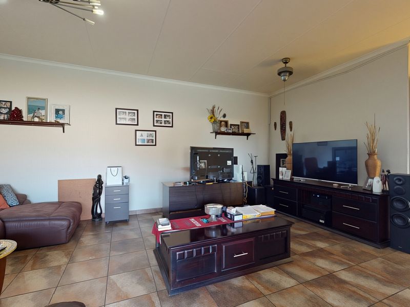 A spacious living room featuring tiled flooring, a ceiling fan, and decorative cove cornicing, offering a comfortable and functional layout for relaxation.