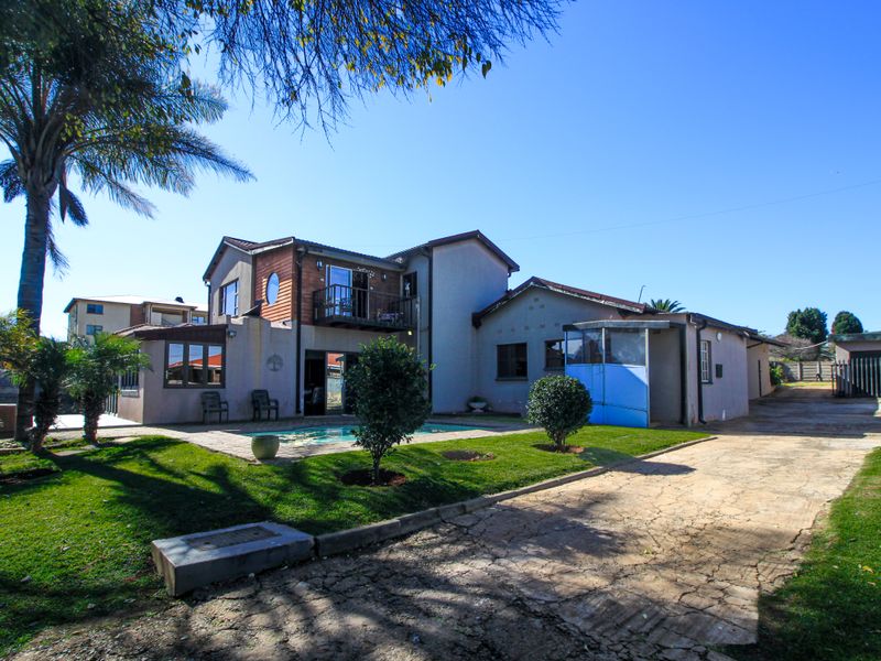Rear view of the property featuring a swimming pool, landscaped garden, paved driveway, and a balcony attached to the upper level.
