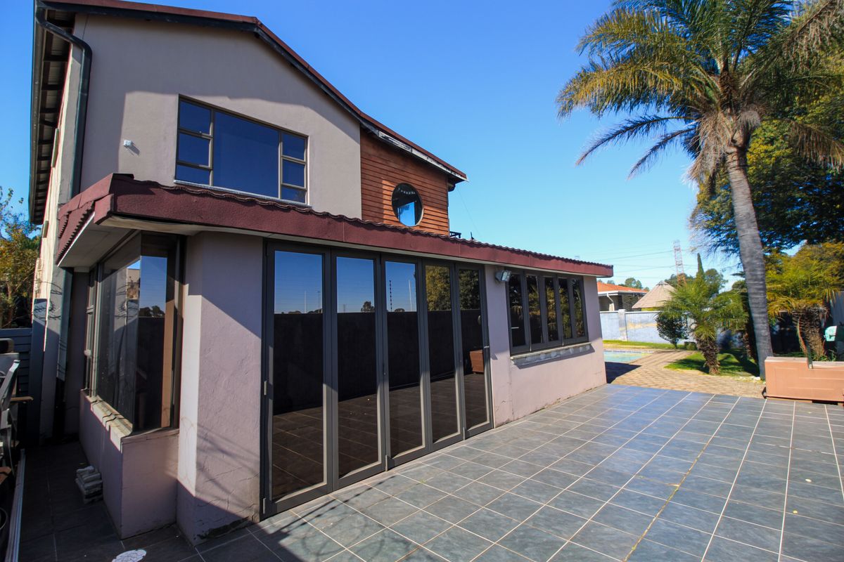 Rear view of the house featuring a spacious tiled patio, modern stacking glass doors, and a well-maintained exterior facade.