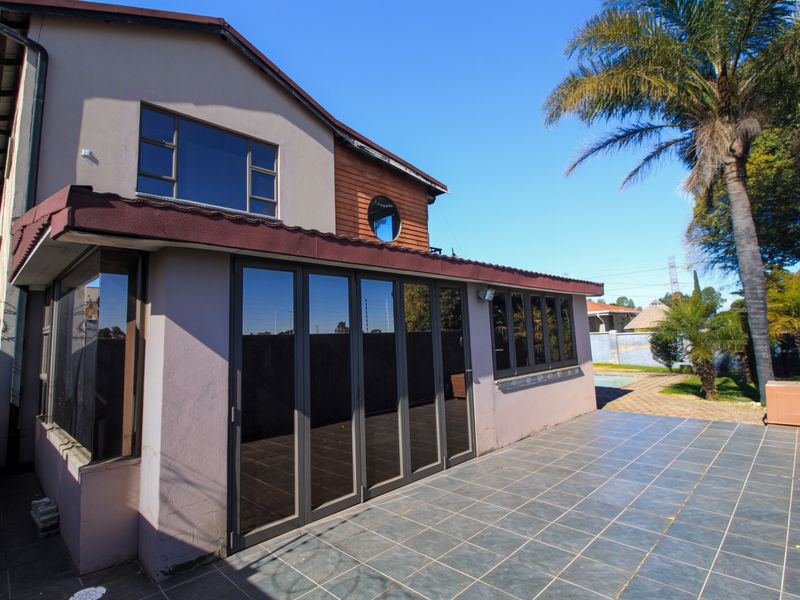 Rear view of the house featuring a spacious tiled patio, modern stacking glass doors, and a well-maintained exterior facade.