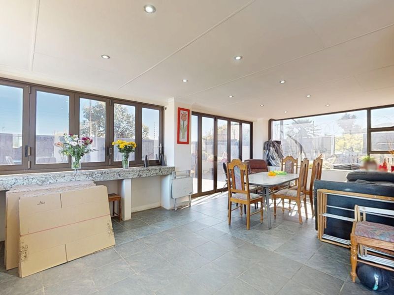 Spacious open-plan living and dining area featuring large aluminium windows, sliding doors, tiled flooring, and a built-in granite countertop.
