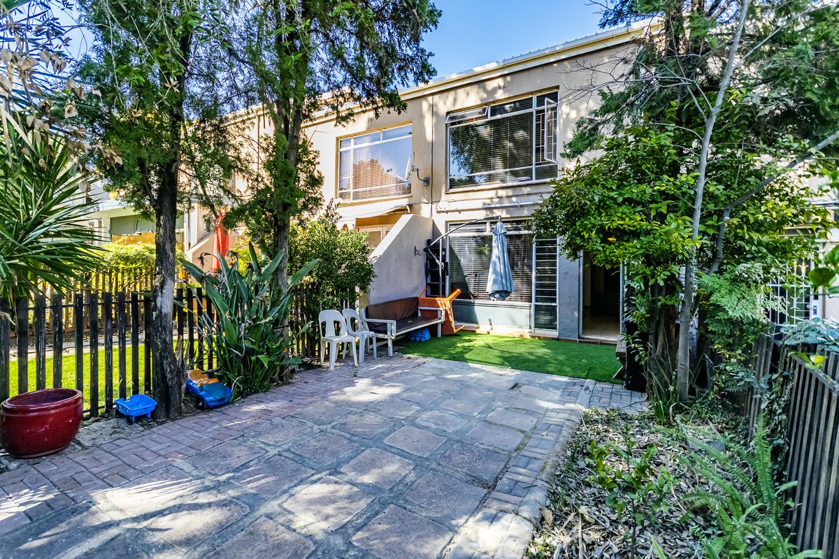Rear exterior view of the townhouse featuring a paved patio area, artificial lawn, and established garden borders with timber fencing.