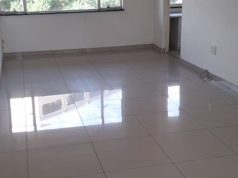 A spacious, empty living area featuring neutral tiled flooring and a large window, providing a blank canvas for interior design.