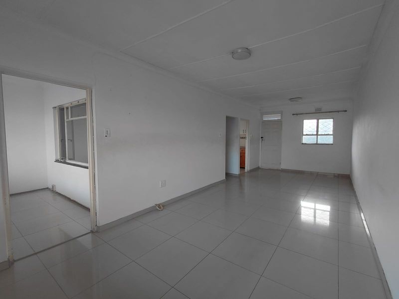 A spacious, empty living area featuring neutral tiled flooring and white walls, providing a blank canvas for interior design and personalization.