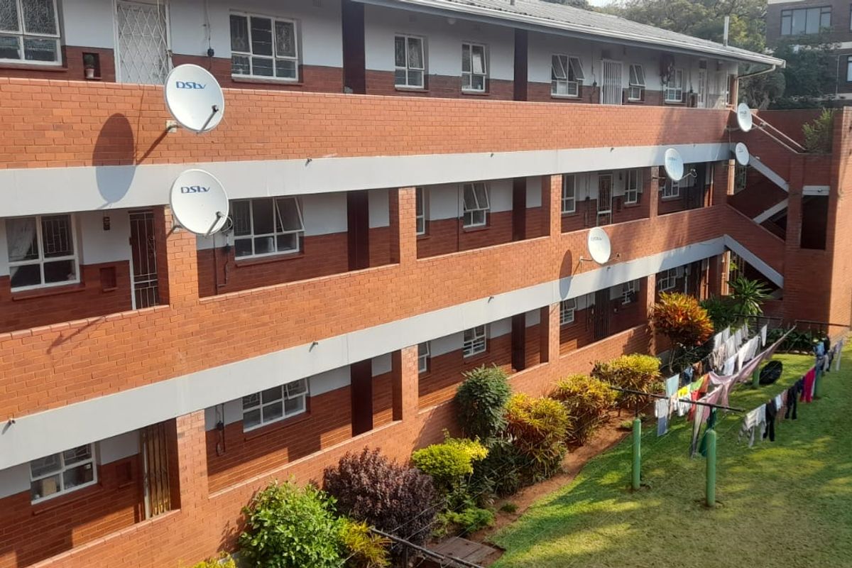 Exterior view of a multi-story apartment complex featuring face brick construction, communal garden space, and external access walkways with security gates.