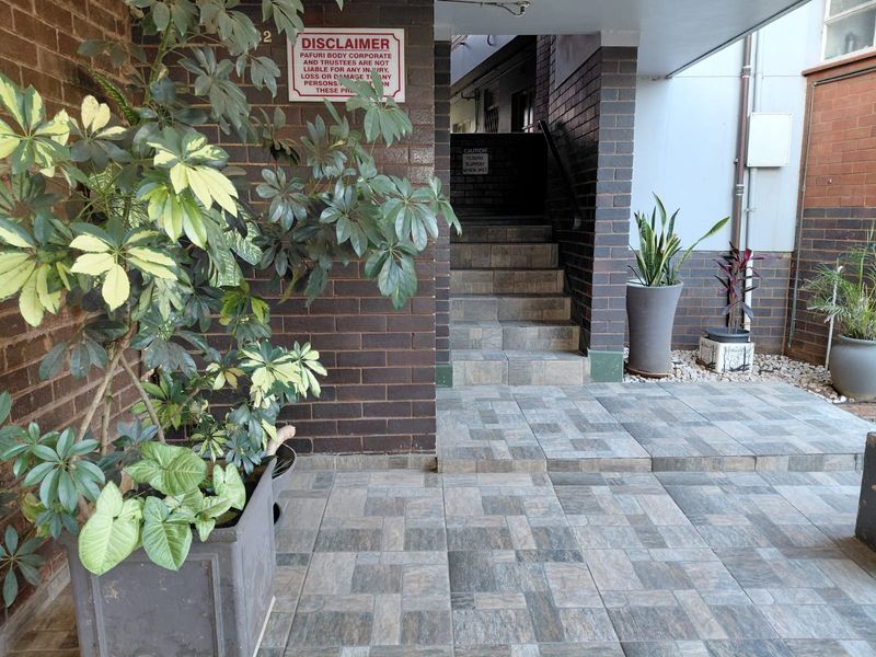A paved entrance area featuring brick walls and a staircase leading to the apartment building interior.
