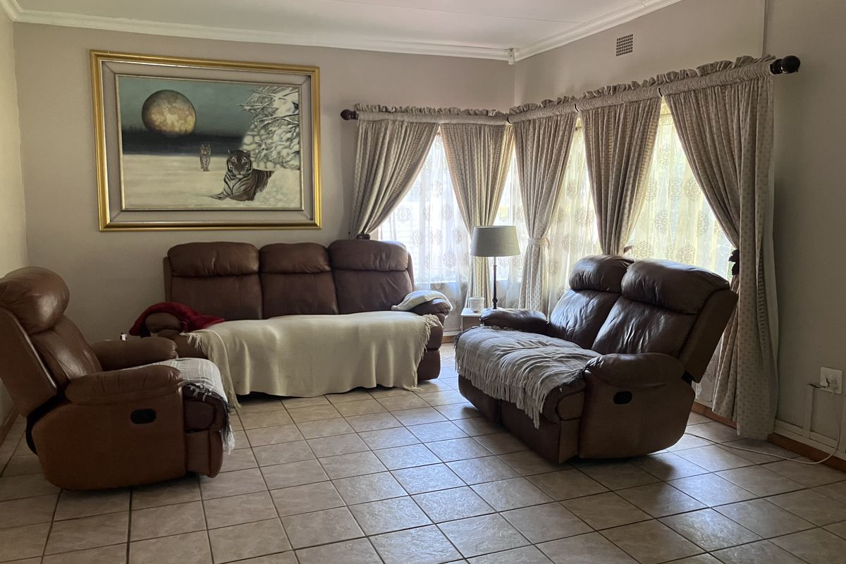 A spacious living room featuring neutral wall tones, tiled flooring, and large windows with classic drapery, offering a comfortable and functional living space.